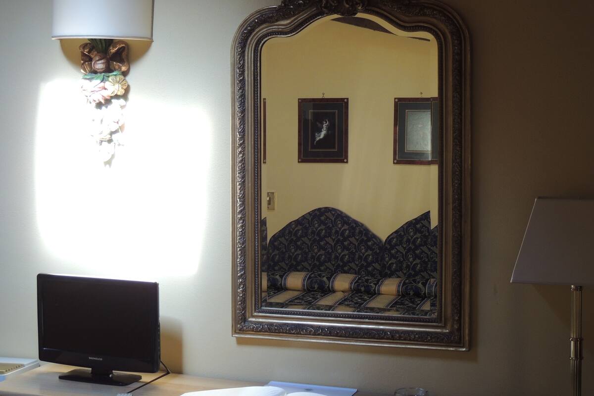 A room with a bed, a flat-screen TV, a wall-mounted lamp, and a large mirror.