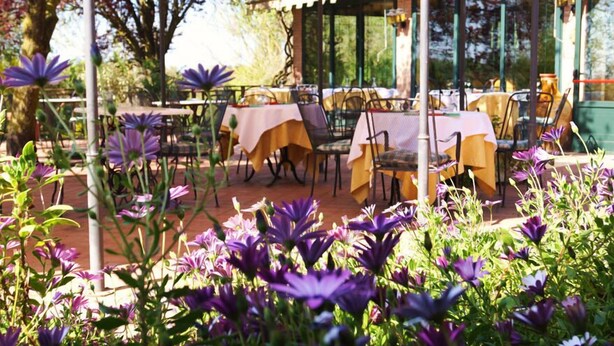 An outdoor dining area with tables and chairs, surrounded by purple flowers.