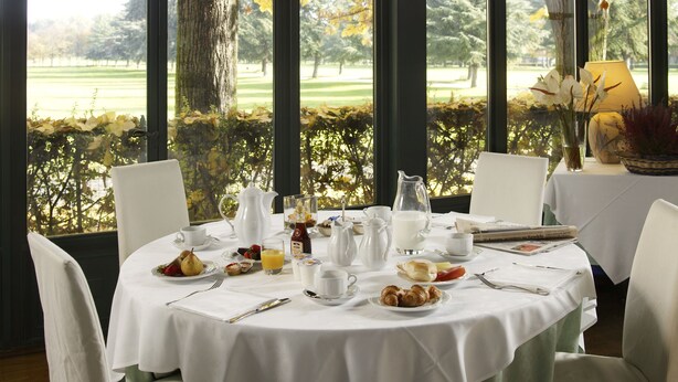 A breakfast table set with plates, cutlery, and beverages, overlooking a golf course. - Hotel Parco Borromeo (Cesano Maderno)