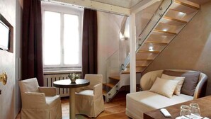 A modern hotel room with a wooden floor, a round table with chairs, a sofa, and a staircase with glass railings. - Hotel Parco Borromeo (Cesano Maderno)