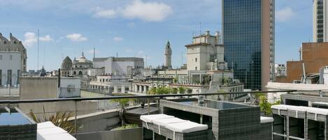 A rooftop terrace with outdoor seating, a view of historic buildings, and a modern skyscraper in the background.
