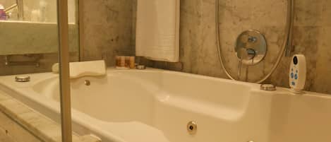 A modern bathroom with a large bathtub, a glass shower enclosure, and a marble-tiled wall.