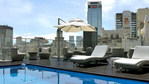 A rooftop pool area with lounge chairs and an umbrella, overlooking a cityscape with modern buildings. - 725 Continental (Buenos Aires)