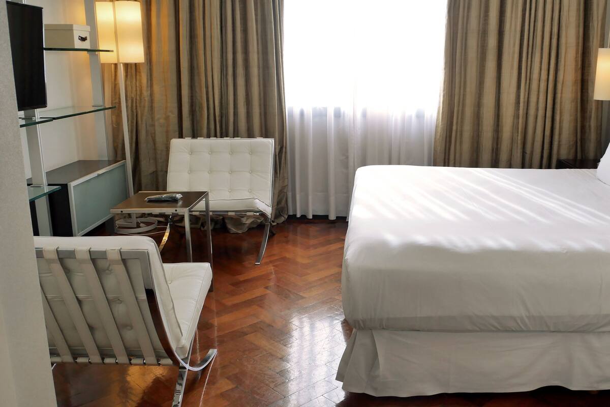 A hotel room with a bed, a chair, a small table, a TV, and curtains.