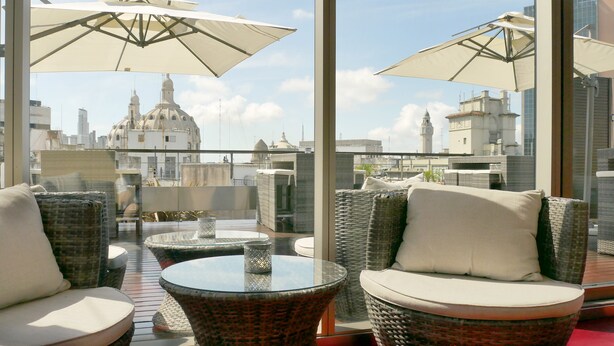 A rooftop terrace with wicker furniture, glass tables, and large umbrellas. - 725 Continental (Buenos Aires)