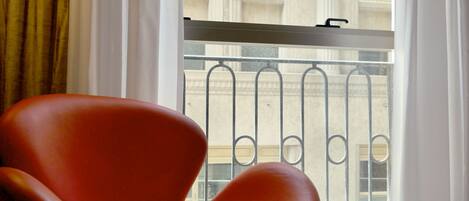 A red chair by a window with a view of a building with classical architecture.