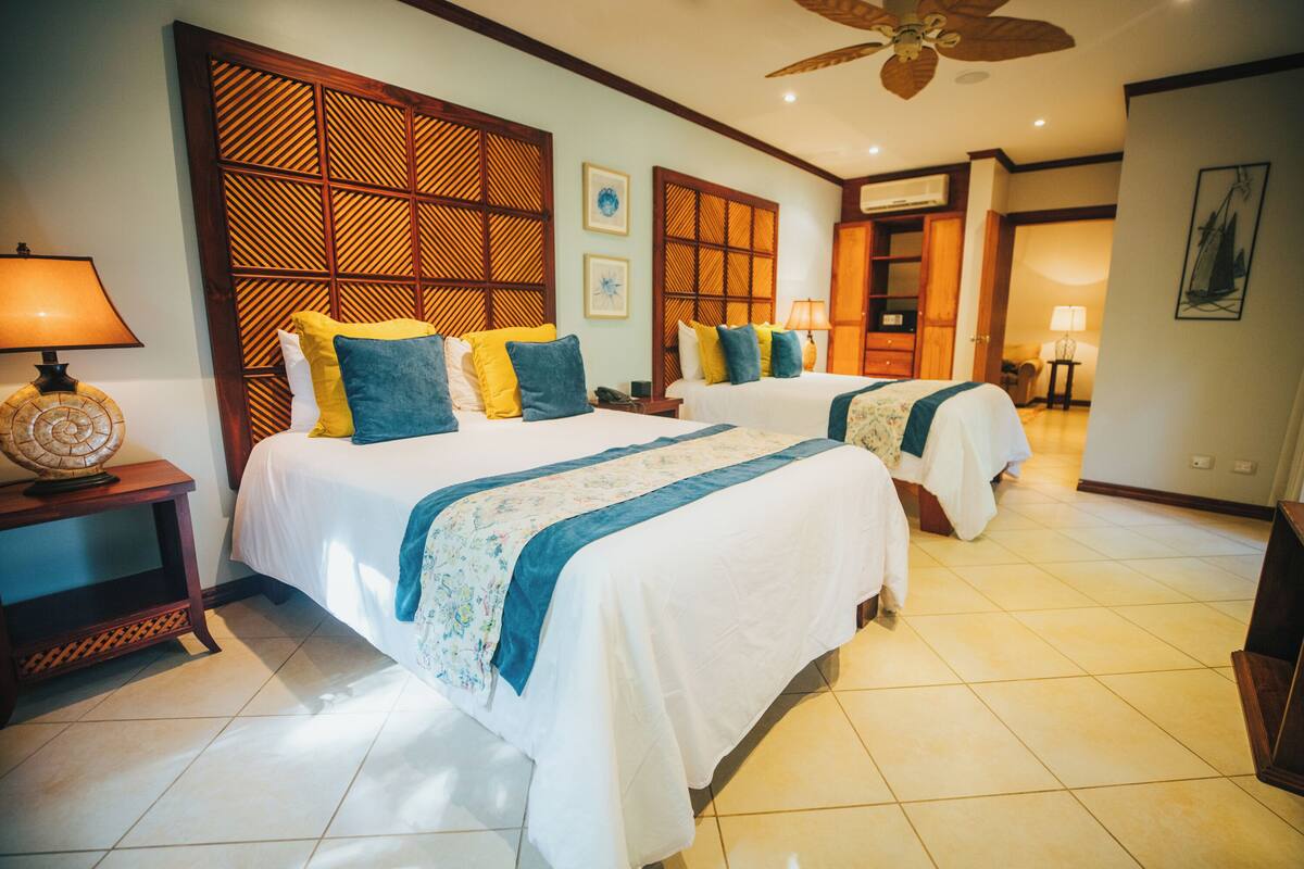 A hotel room with two beds, a wooden partition wall, a ceiling fan, and a tiled floor.