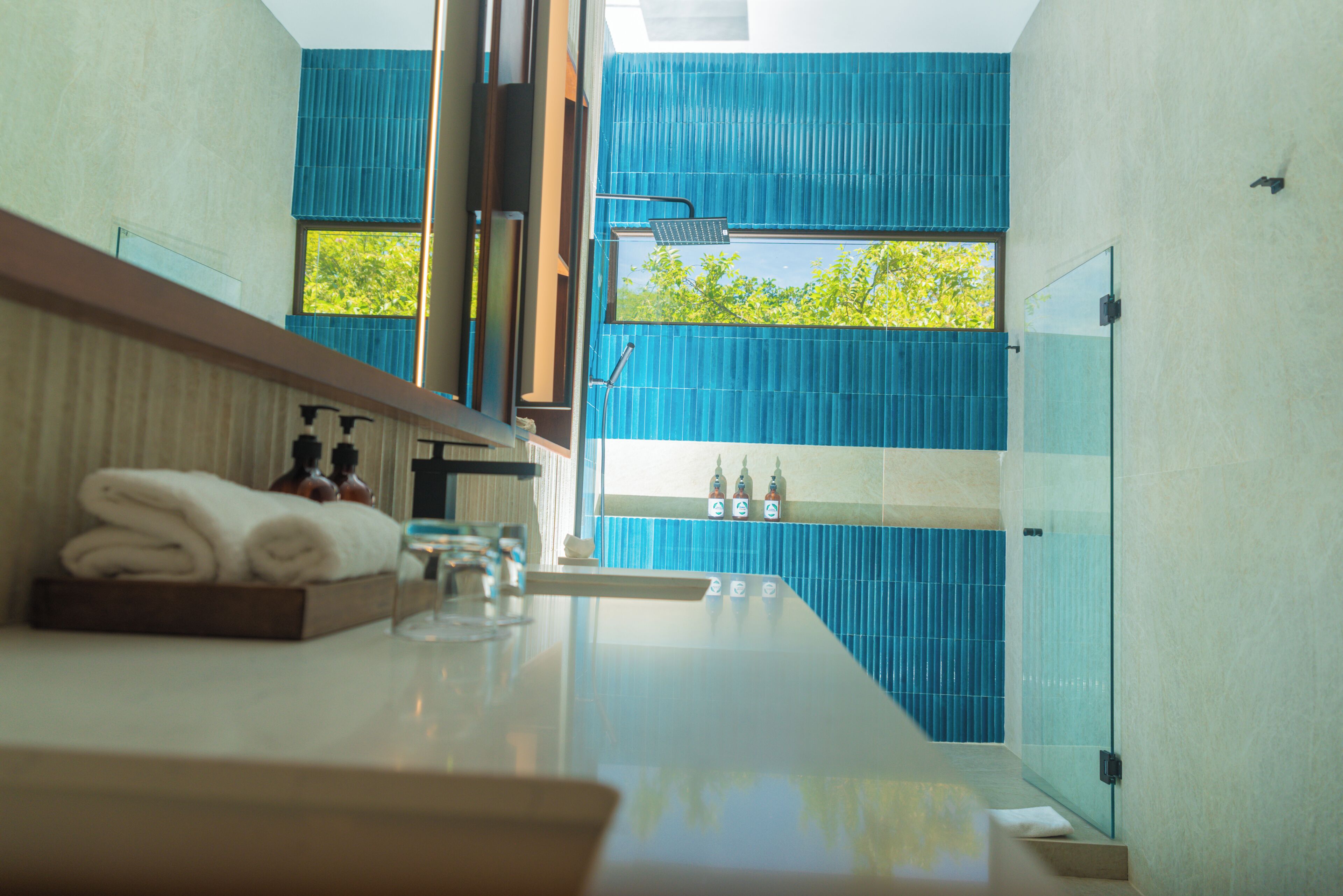 A modern bathroom with a glass shower enclosure, a towel rack, and a window with a view of trees.