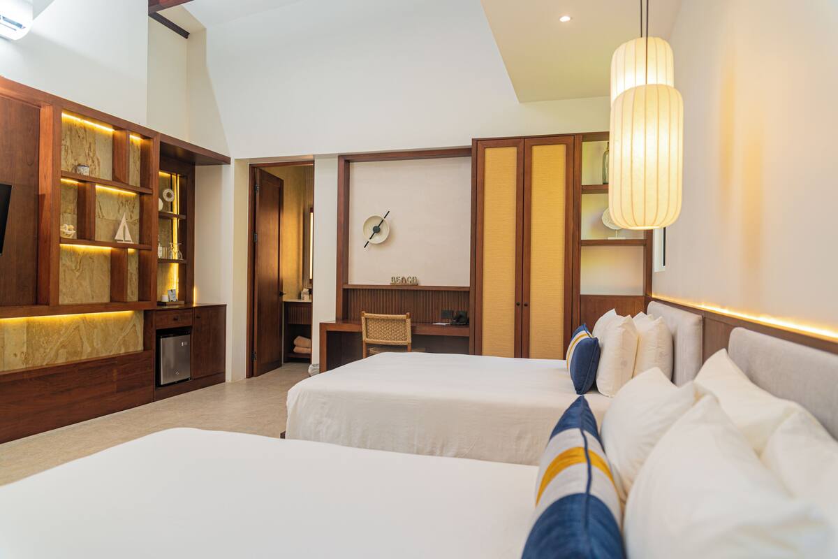 A hotel room with two beds, a wooden cabinet with shelves, a desk, and a chair.
