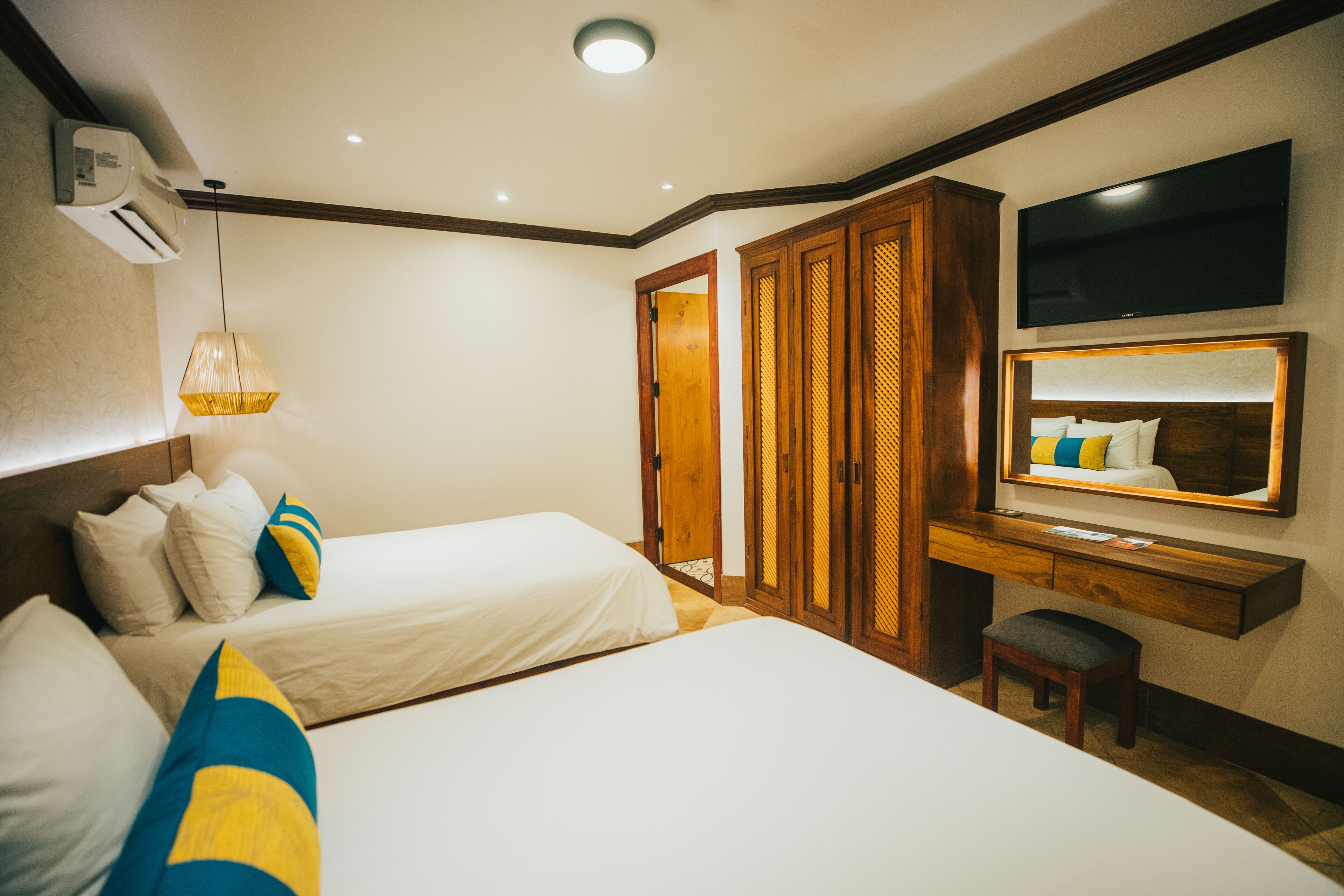 Habitación de hotel con dos camas, un armario de madera, un escritorio con espejo y un televisor.