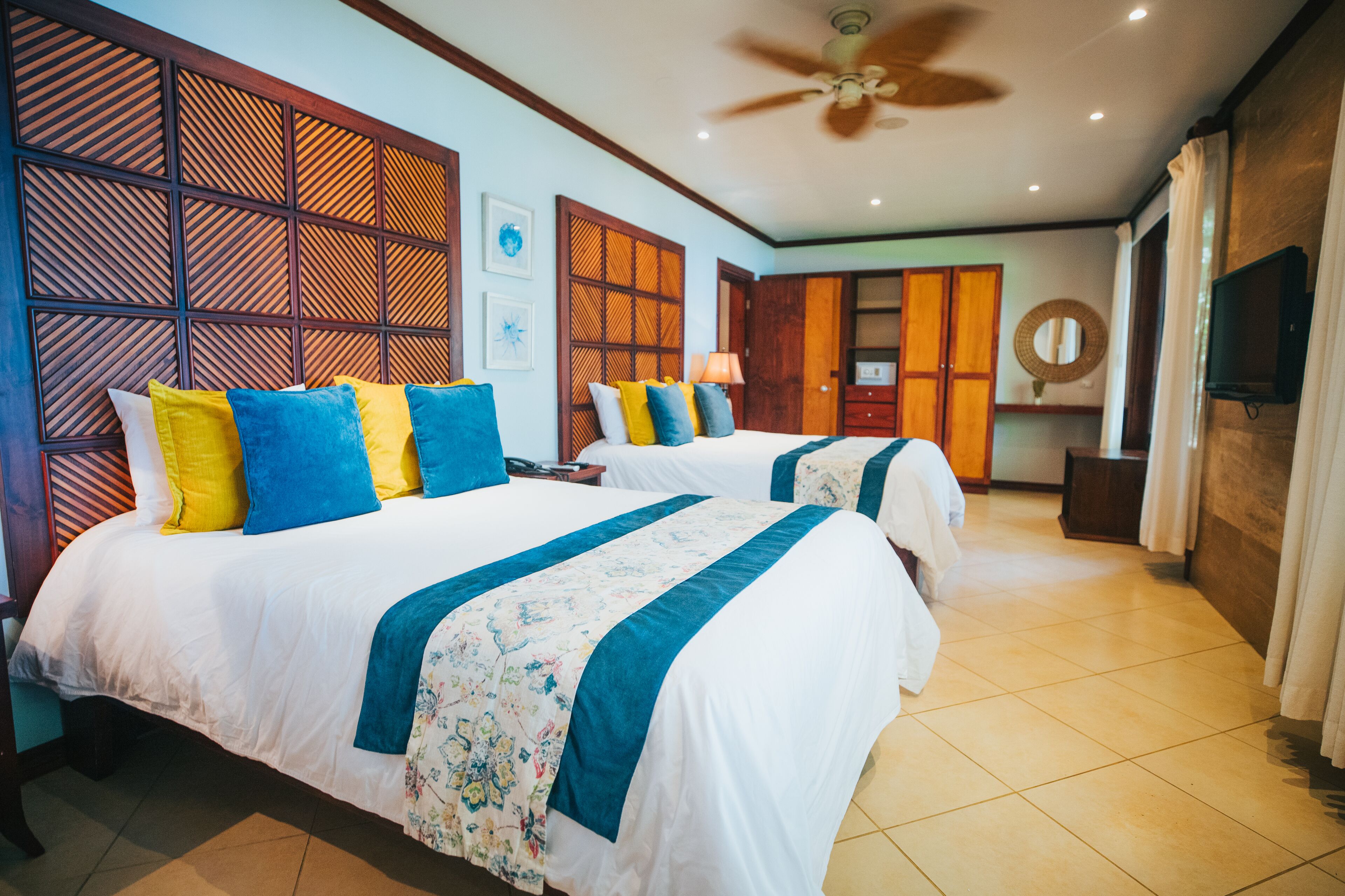 A hotel room with two beds, a ceiling fan, a TV, and a wooden partition wall.