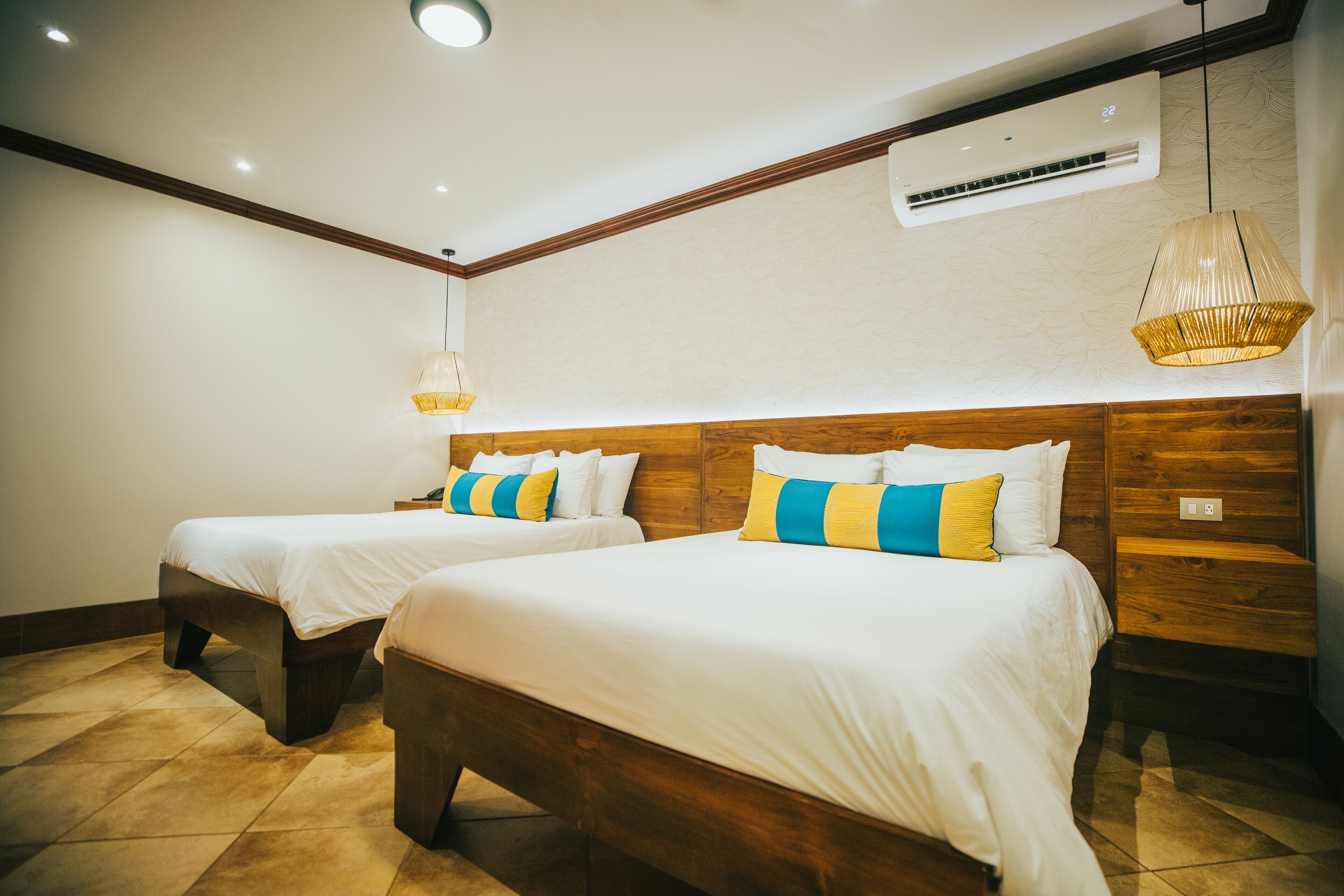 A hotel room with two beds, wooden headboards, white bedding, and a hanging light fixture.