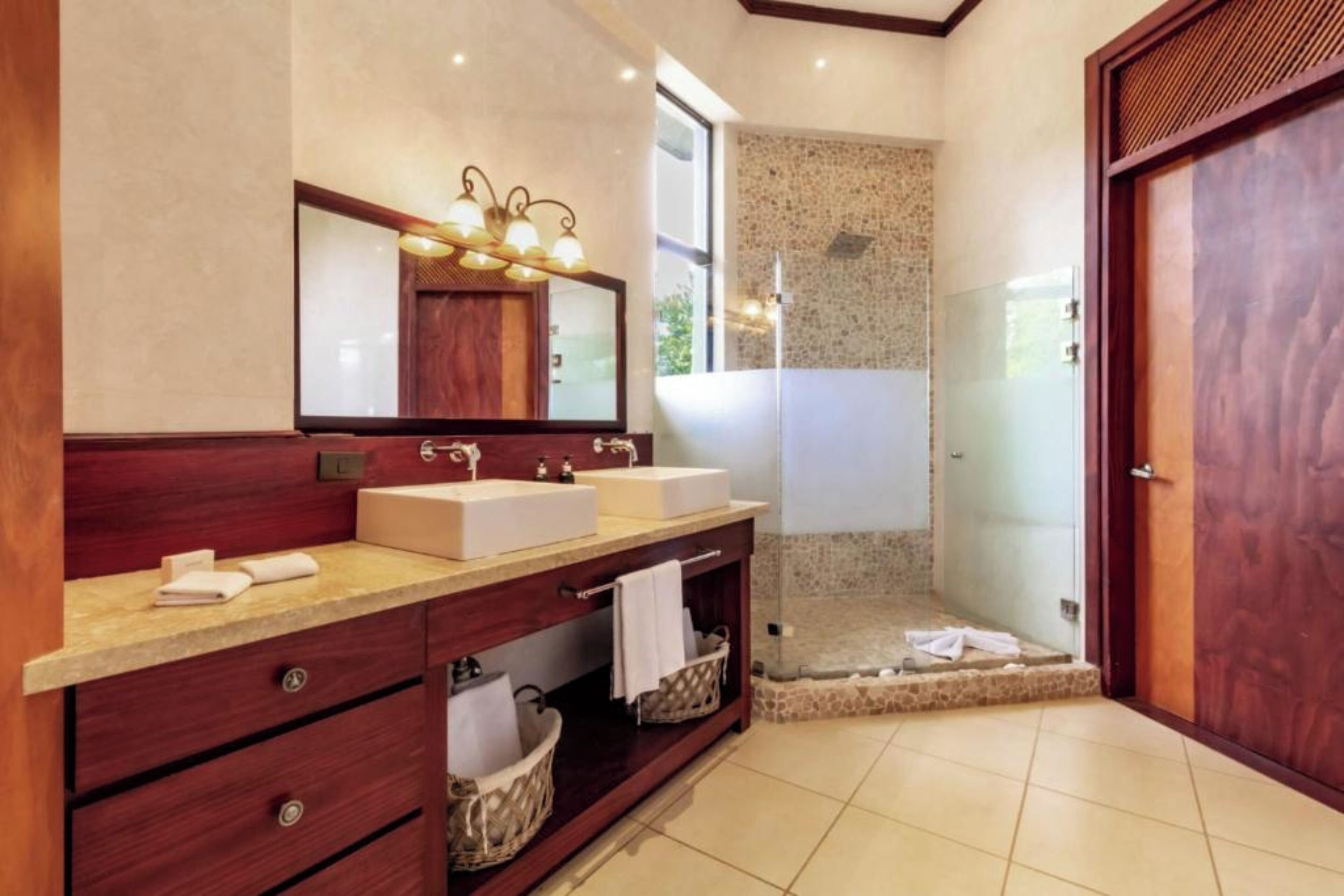 Un baño moderno con dos lavamanos, un espejo grande y una ducha con mampara de vidrio.