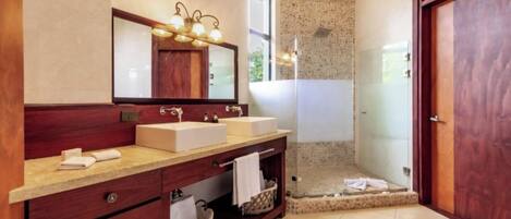 A modern bathroom with two sinks, a large mirror, and a glass-enclosed shower.