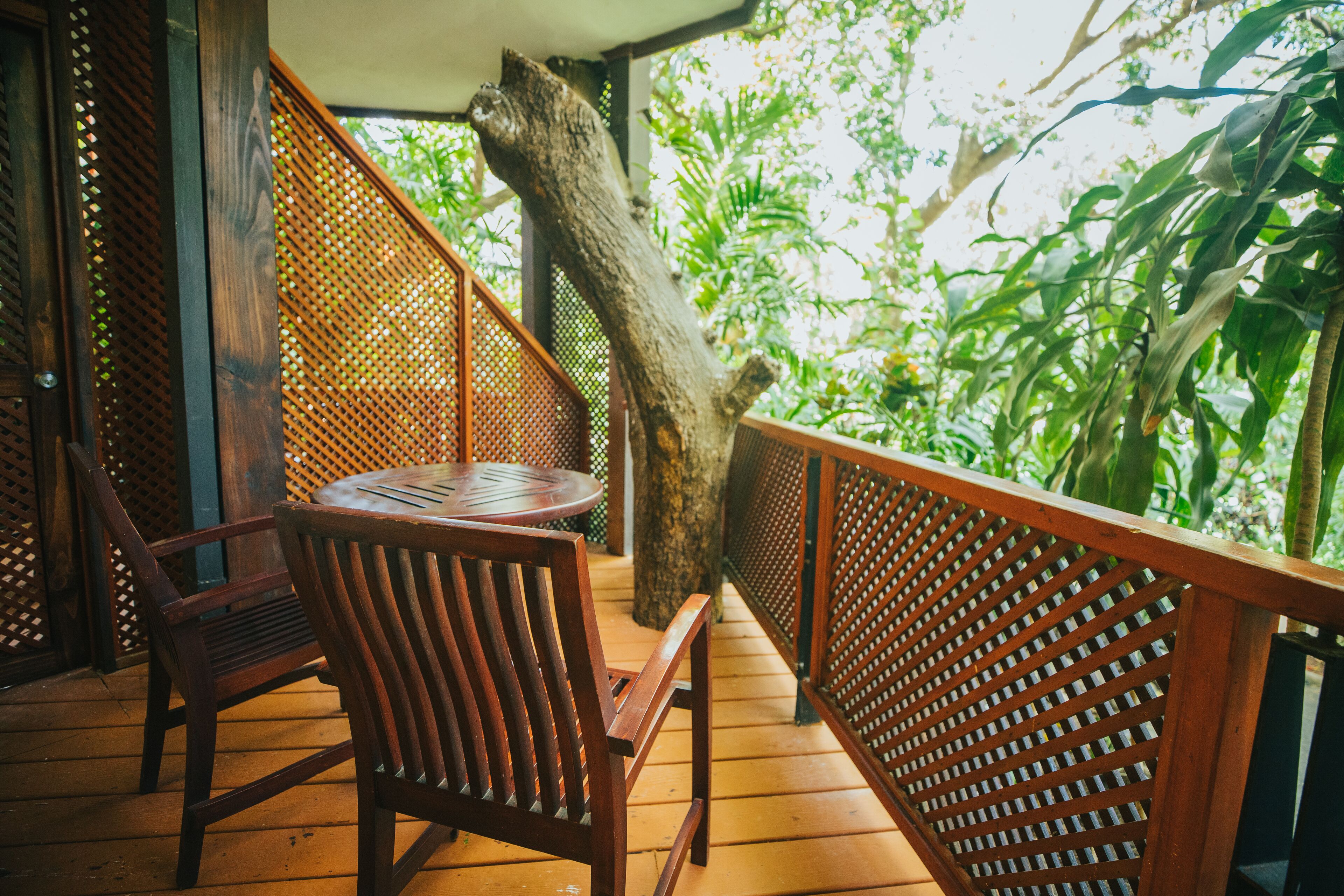 A wooden deck with a round table and chairs, surrounded by a wooden fence and lush greenery.
