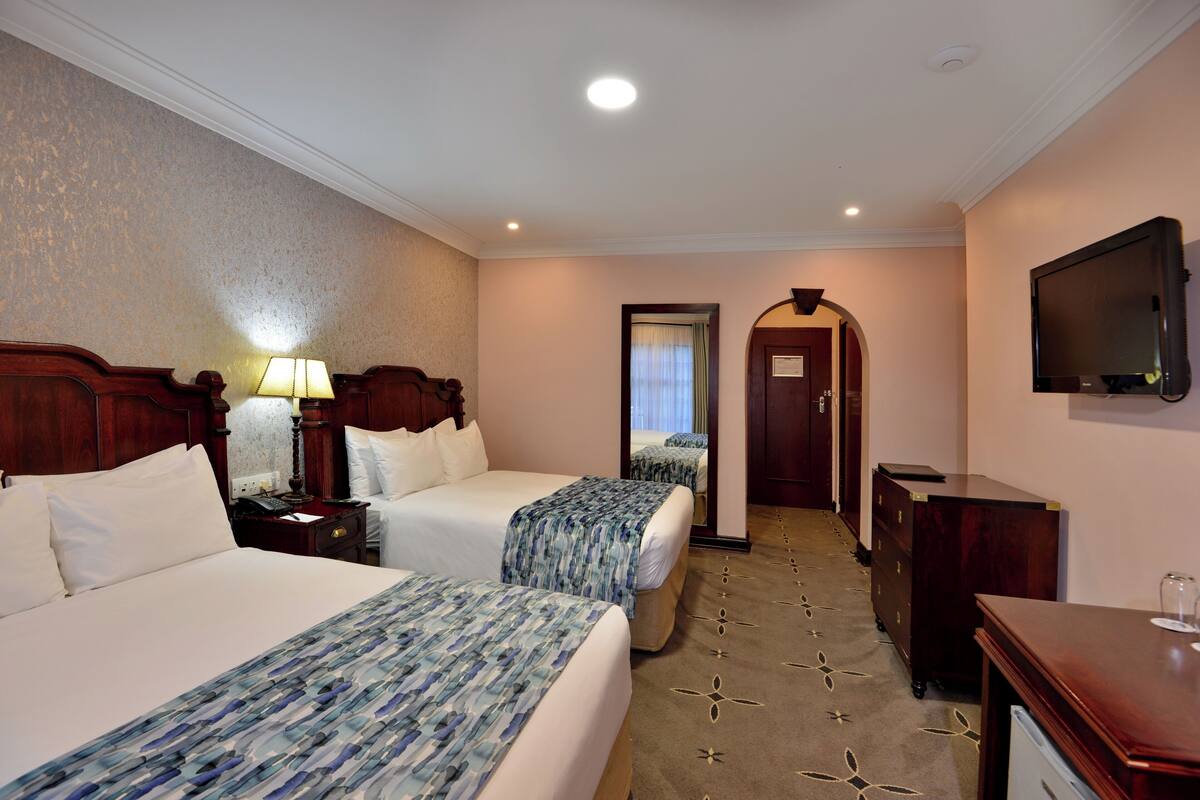 A hotel room with two beds, a television, a desk, and a dresser.