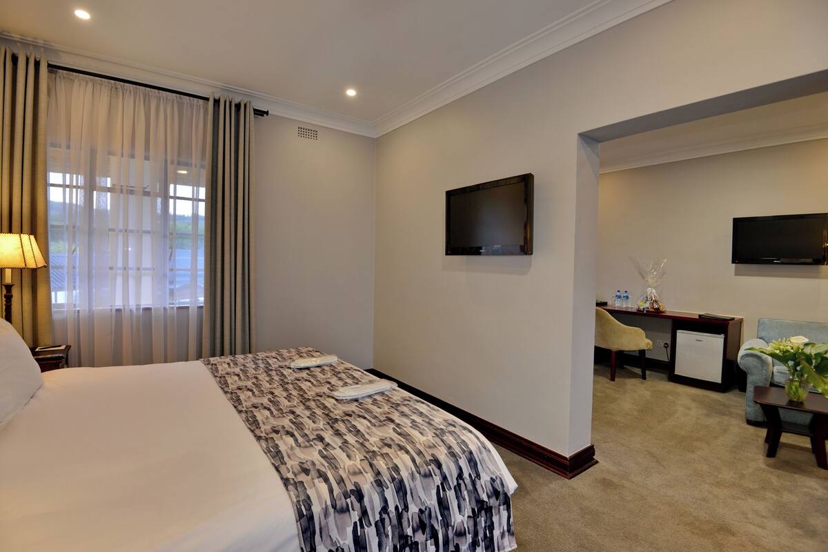 A hotel room with a large bed, a desk with a chair, a television, and a small refrigerator.
