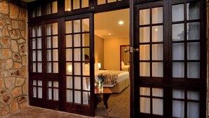 A hotel room with a stone wall, a bed with a floral bedspread, and a nightstand with a vase. - Troutbeck Resort (Nyanga)