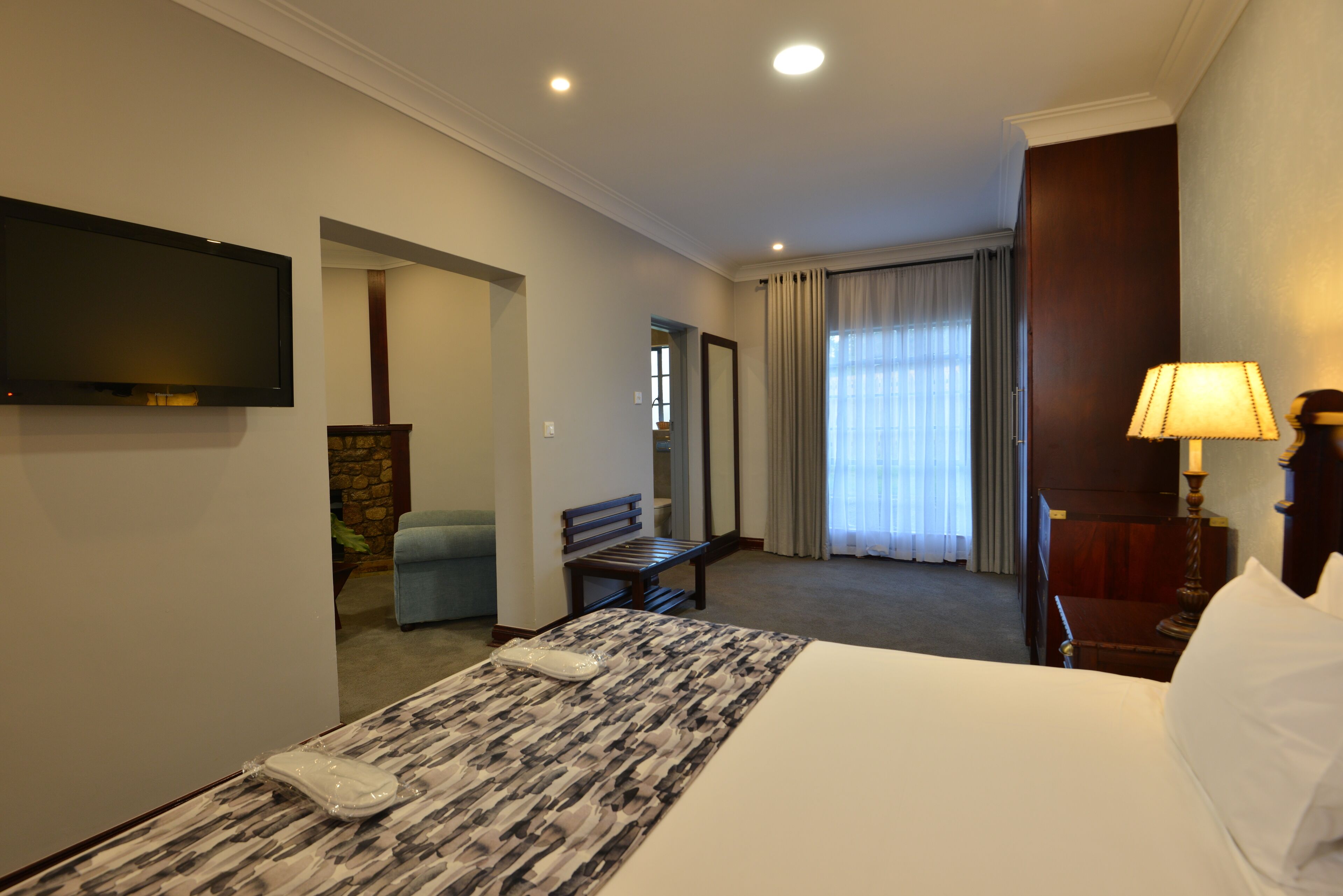 A hotel room with a bed, a desk with a lamp, a chair, a television, and a window with curtains.