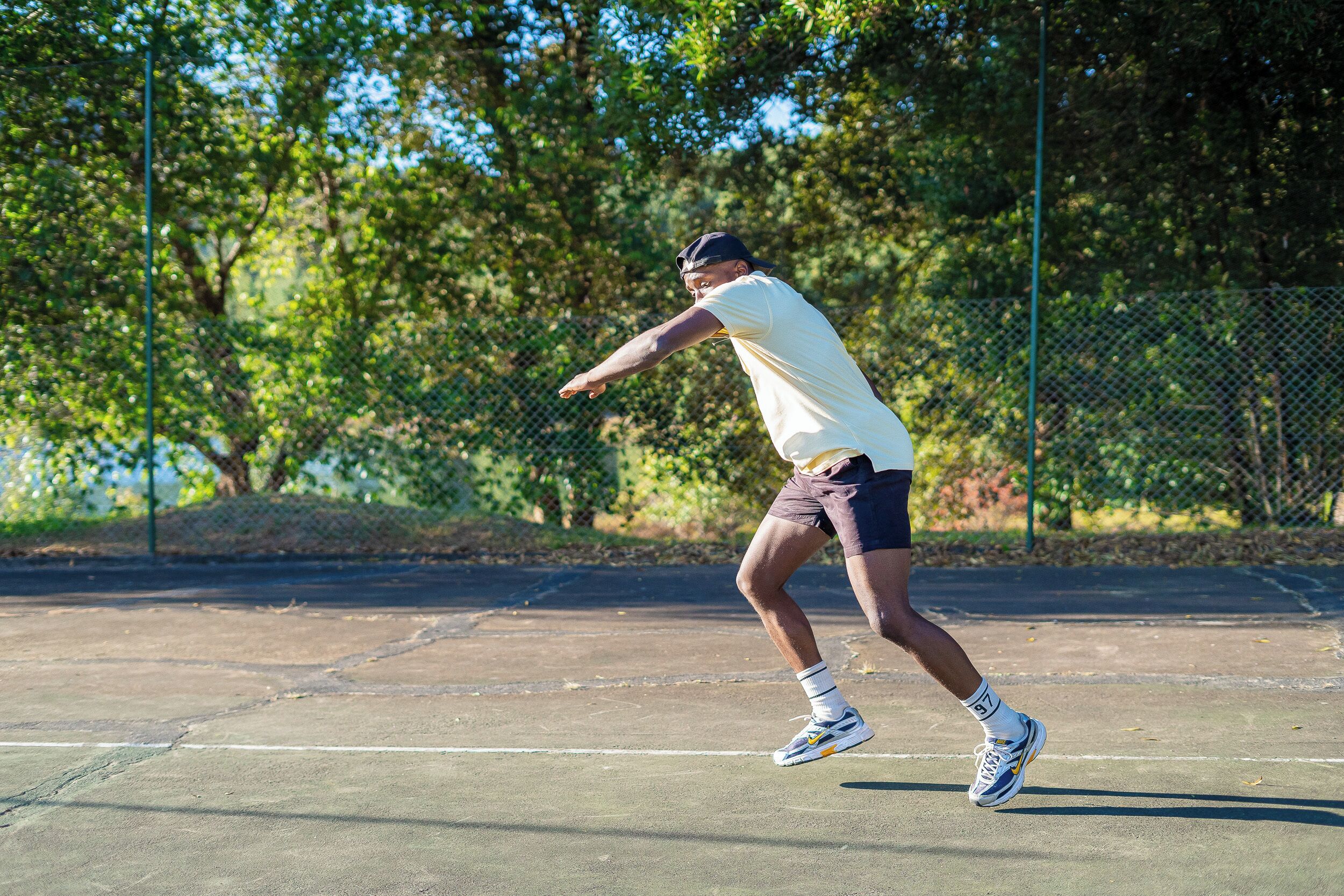Una persona jugando tenis en una cancha al aire libre con árboles de fondo.