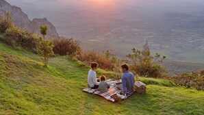 A family picnic on a grassy hill with a view of distant mountains and a valley. - Troutbeck Resort (Nyanga)