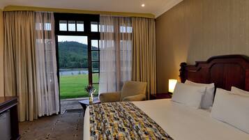 Habitación de hotel con una cama grande, una silla, un escritorio y vistas a un paisaje verde por la ventana.
