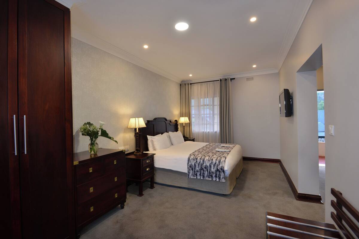 A hotel room with a large bed, a dresser with drawers, a nightstand with lamps, and a TV mounted on the wall.