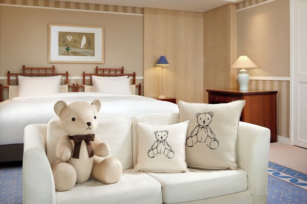 A hotel room with a bed, a sofa with a teddy bear, and two pillows with bear designs.