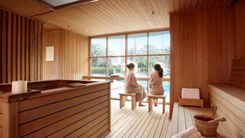 Une salle de spa en bois, équipée de deux bancs, d’un comptoir d’accueil et d’une grande fenêtre donnant sur des palmiers.