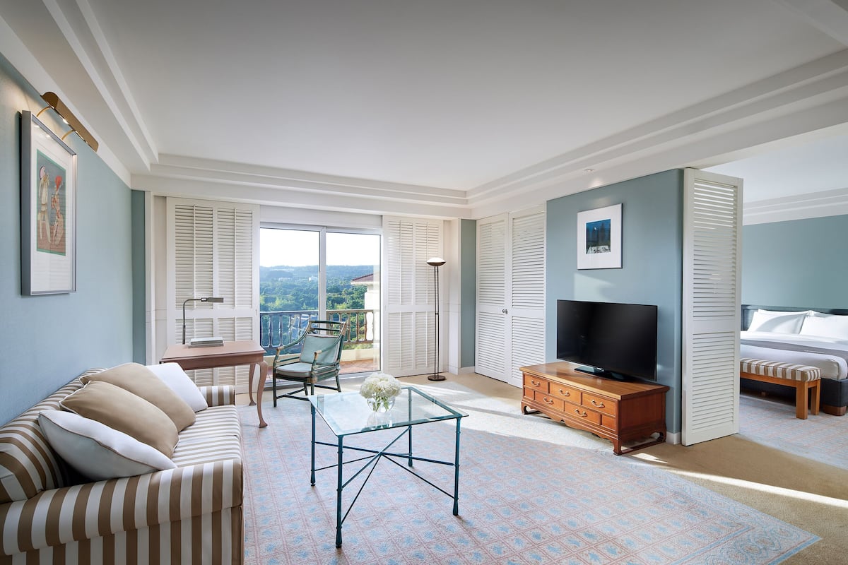 A spacious living room with a sofa, a glass coffee table, a TV, and a balcony with a view.