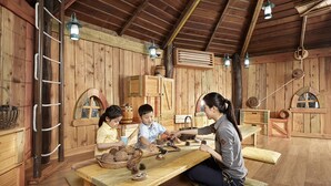 A rustic wooden room with a high ceiling, wooden walls, and a long table where three people are engaged in an activity. - The Shilla Jeju (Seogwipo)