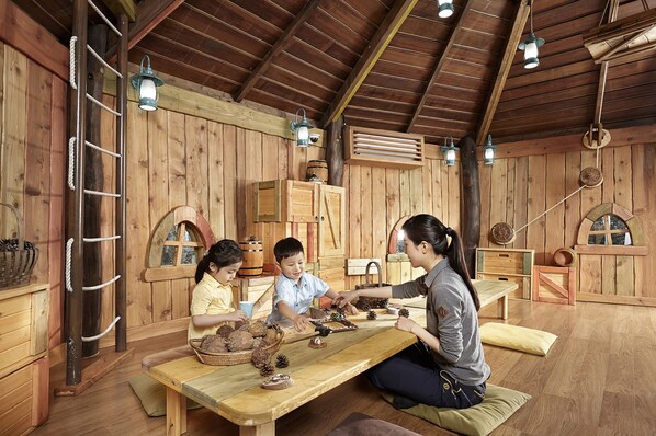 A rustic wooden room with a high ceiling, wooden walls, and a long table where three people are engaged in an activity. - The Shilla Jeju (Seogwipo)