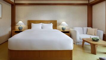 A hotel room with a large bed, two bedside tables with lamps, a white armchair, and a small table with a decorative item.