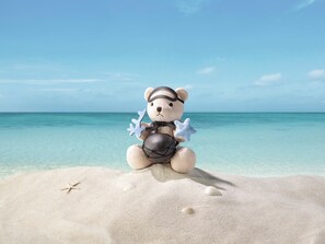 A beach scene with a teddy bear sitting on the sand, holding starfish. - The Shilla Jeju (Seogwipo)