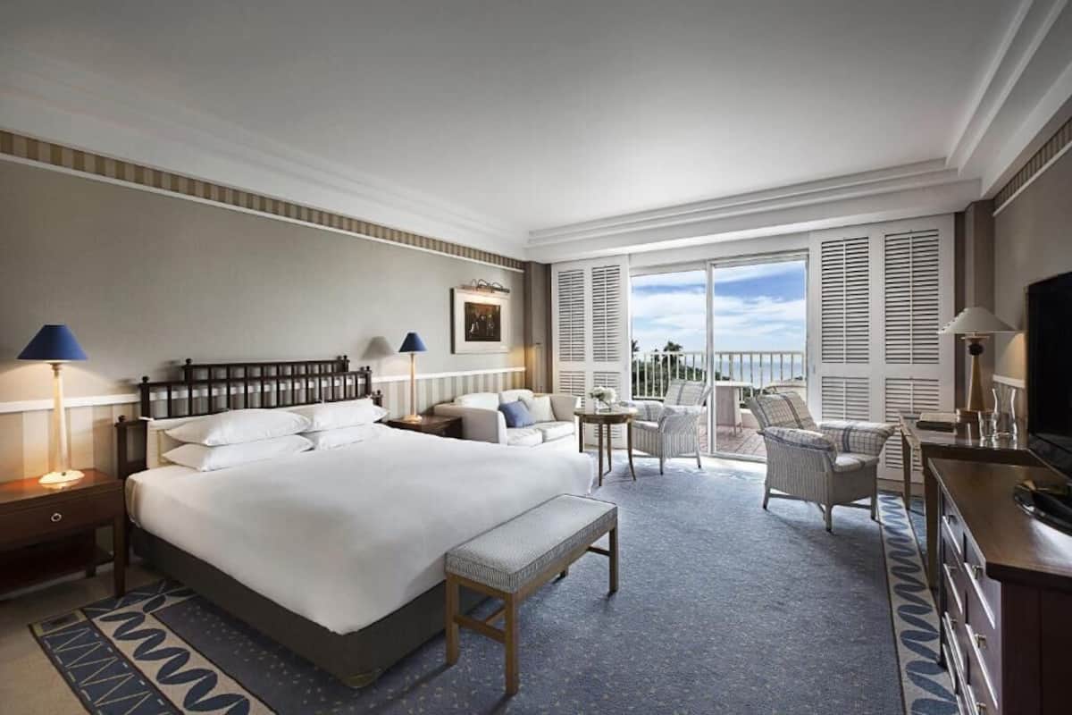 Ein Hotelzimmer mit einem großen Bett, Nachttischen, einem Schreibtisch, einem Sessel, einem kleinen Tisch und einem Fernseher.