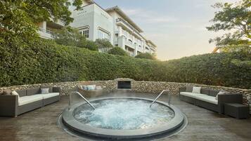 A hot tub surrounded by outdoor seating, a stone wall, and lush greenery.