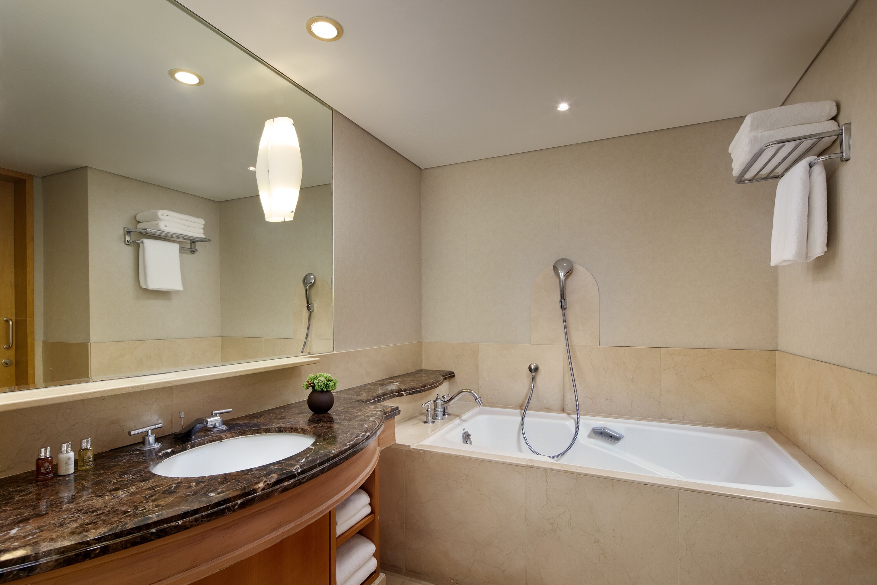 A modern bathroom with a marble sink, a large mirror, a bathtub, and a towel rack.