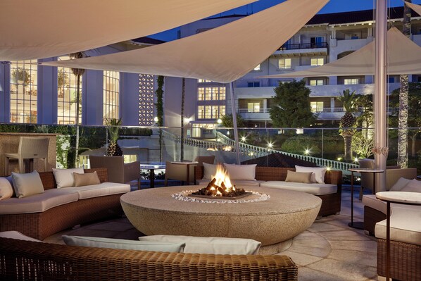 A rooftop lounge with a fire pit, wicker furniture, and a view of the building's balconies.