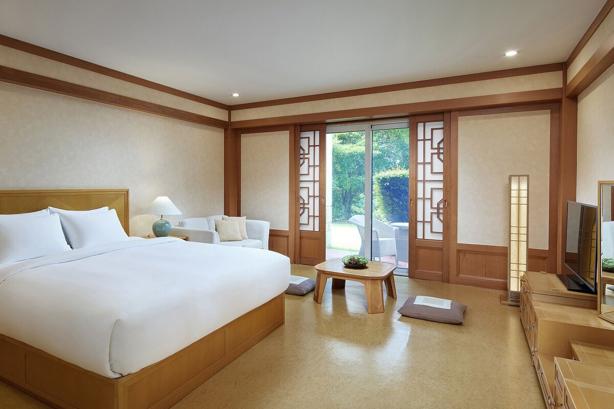 Habitación de hotel con una cama grande, un escritorio, una silla, un televisor y vistas al exterior a través de una puerta corrediza.