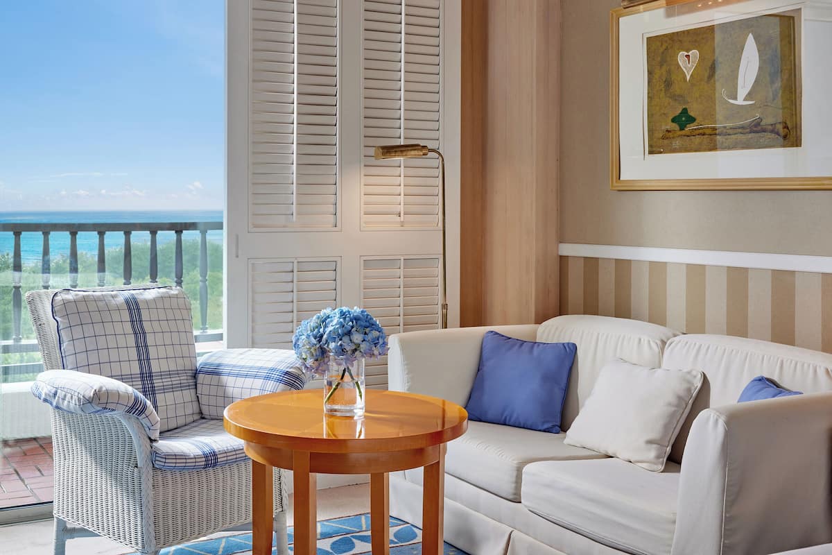 A balcony with a wicker chair, a white sofa, and a table with a vase of flowers.