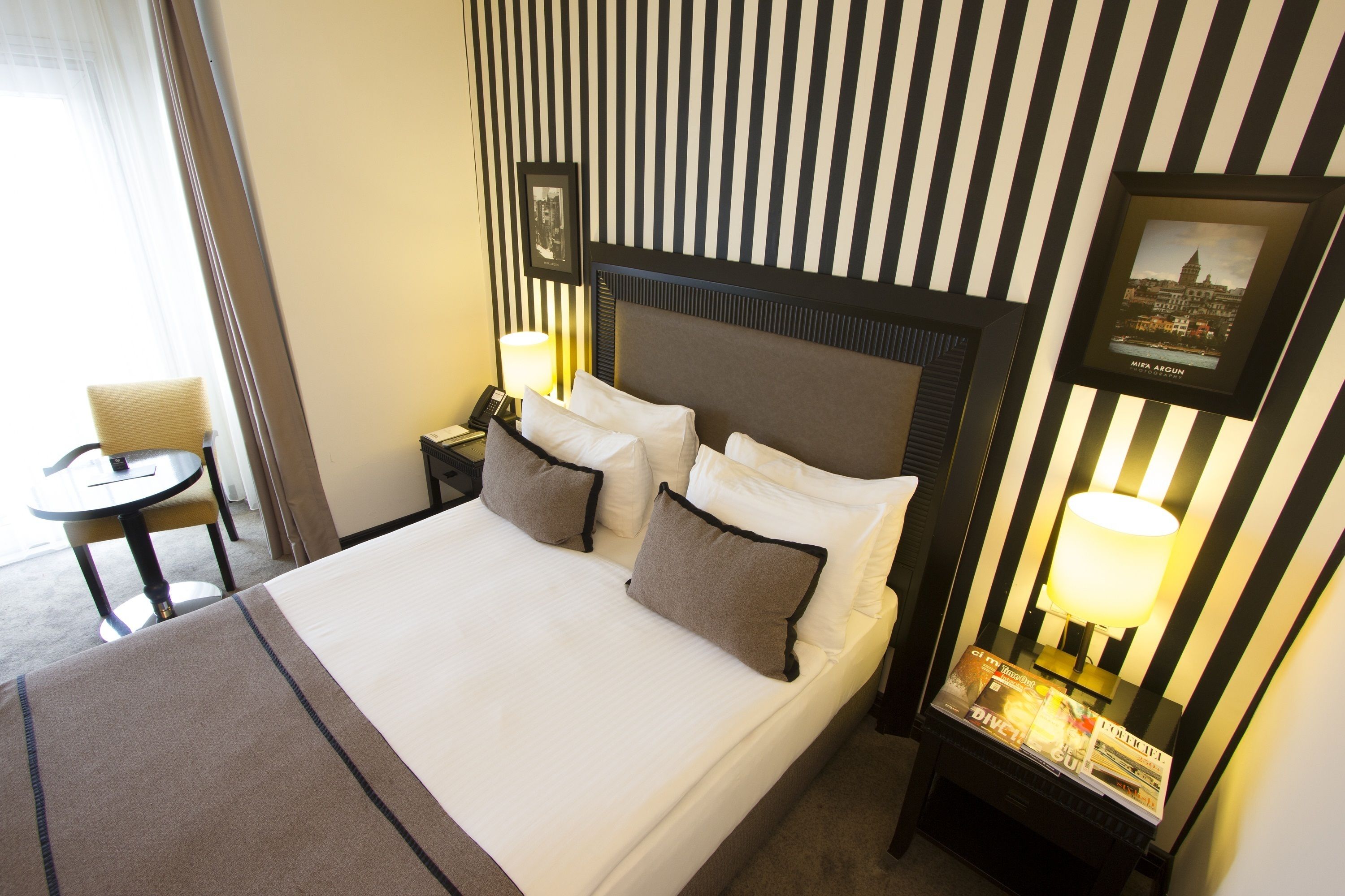 A hotel room with a large bed, a nightstand with a lamp, a chair, and a framed picture on the wall.