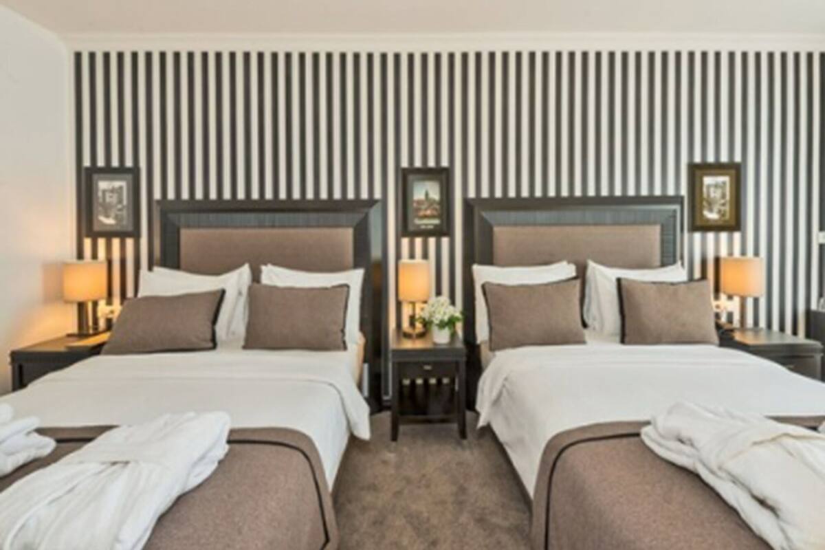 A hotel room with two beds, each with a headboard, bedside tables, lamps, and towels.
