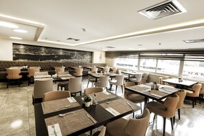 A modern restaurant with multiple dining tables and chairs, a large black mural on the wall, and large windows providing natural light. - Avantgarde Urban Taksim (Istanbul)