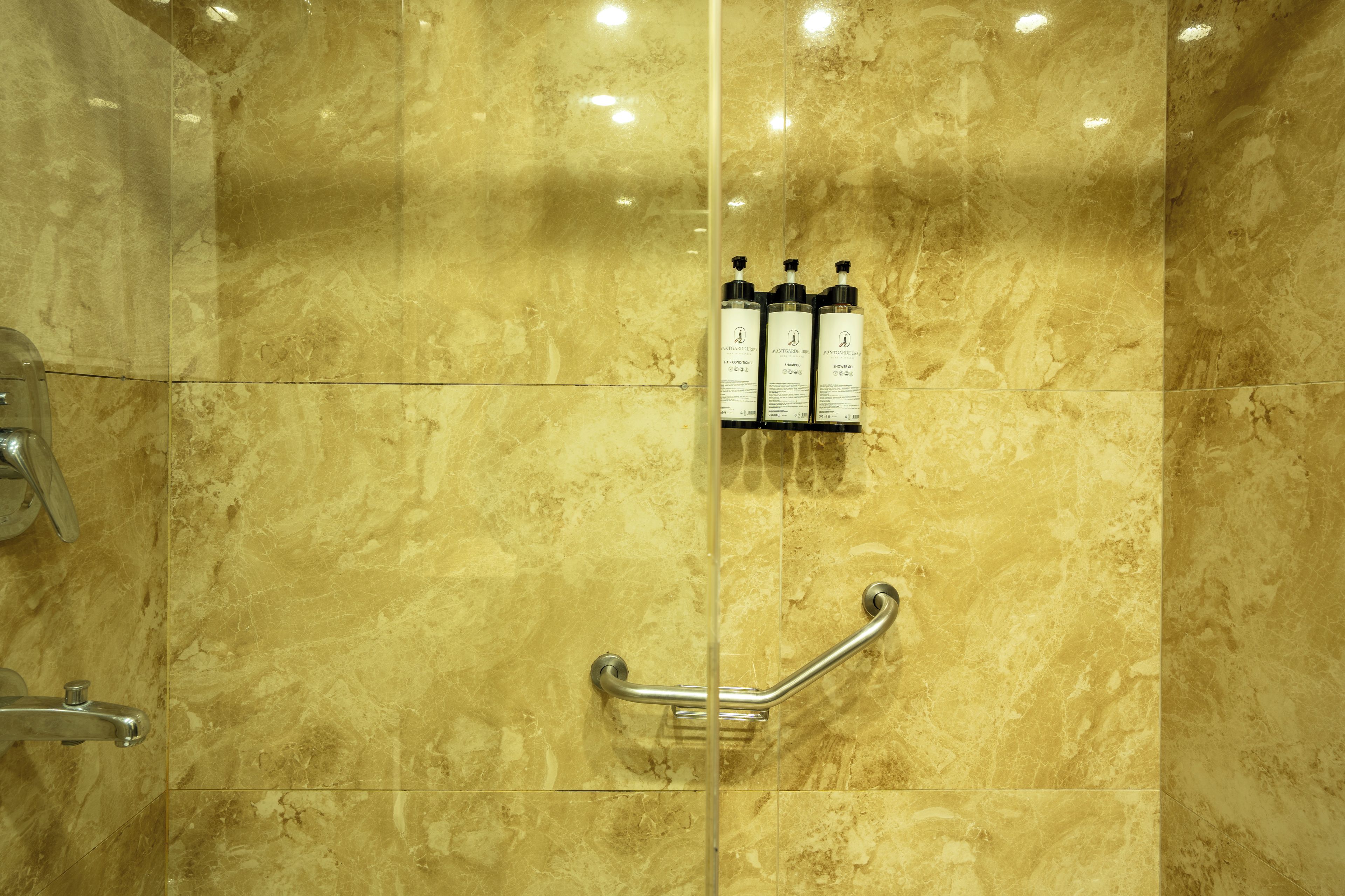 Une salle de bain avec un mur en marbre, une barre d’appui et trois flacons de produits pour les soins capillaires.