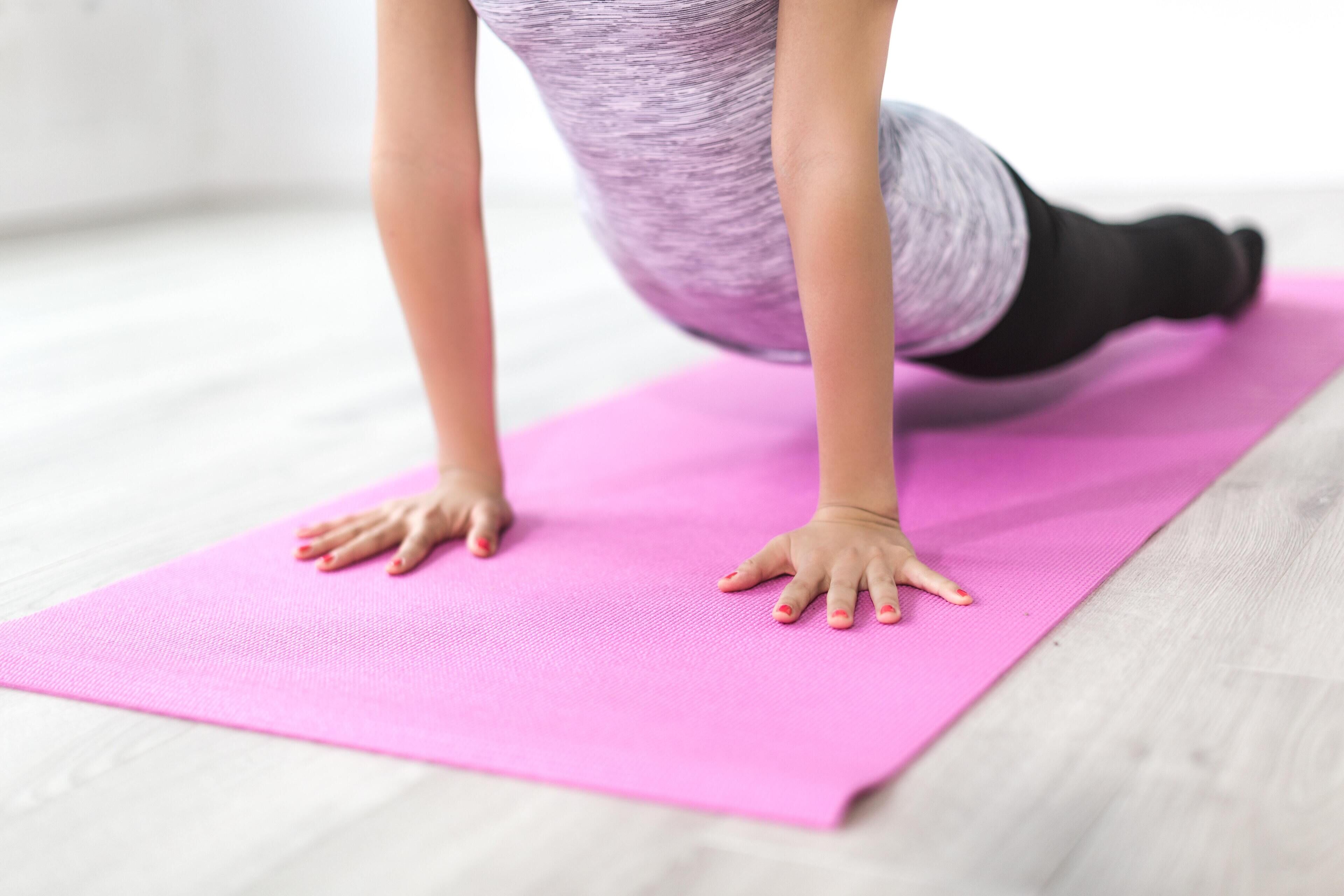 Una persona realizando una postura de yoga sobre una colchoneta rosa.