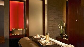 Une salle de spa moderne équipée d’une table de massage, d’un plateau avec du thé et des bougies, et d’un mur éclairé en rouge.