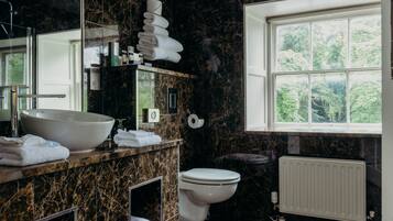 Et moderne badeværelse med en stor vask, toilet og et vindue med udsigt til grønne omgivelser.