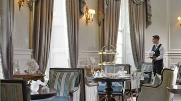 Un comedor formal con muebles elegantes, un camarero sosteniendo una bandeja y decoración clásica.