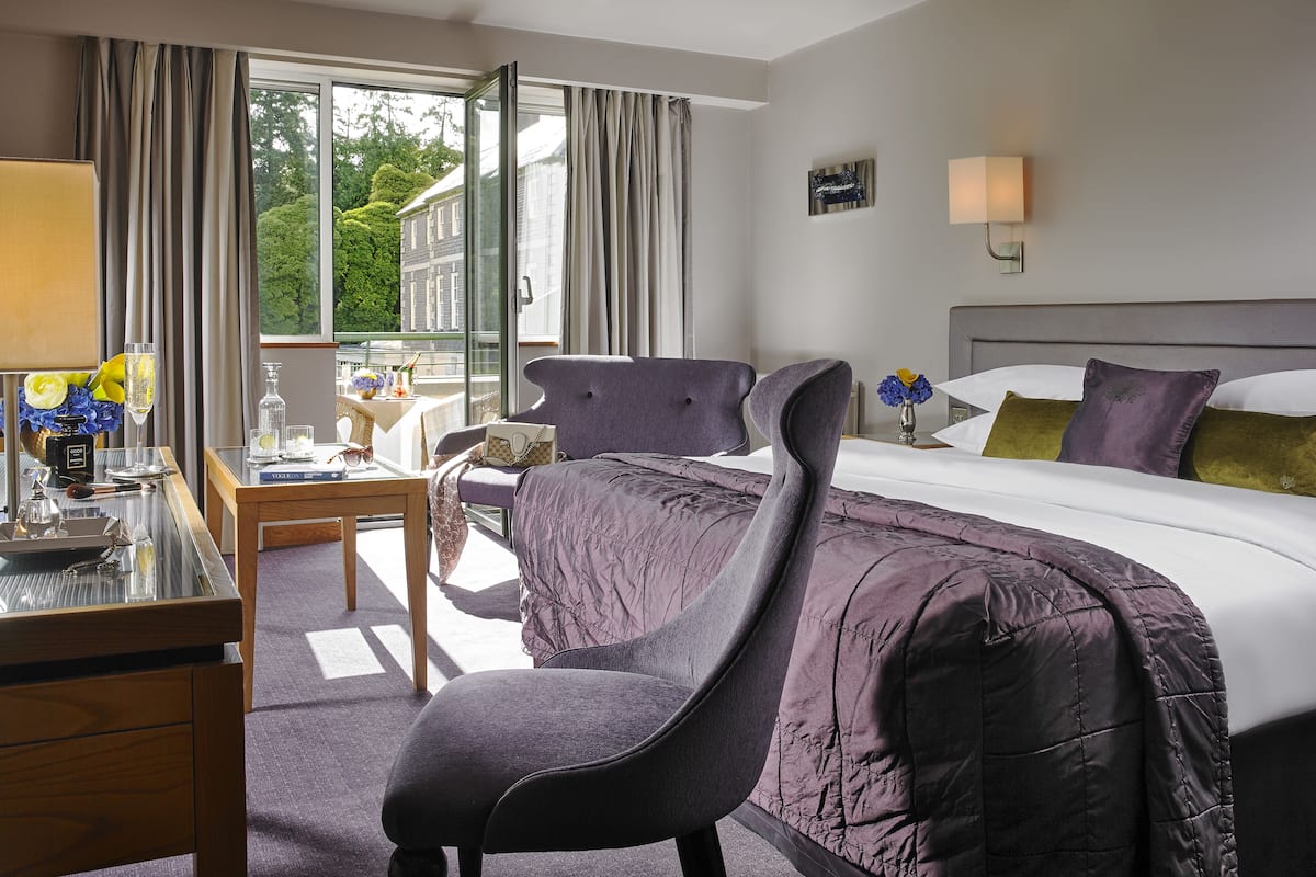 Een hotelkamer met een bed, een bureau met stoel, een raam met gordijnen en uitzicht op groen.