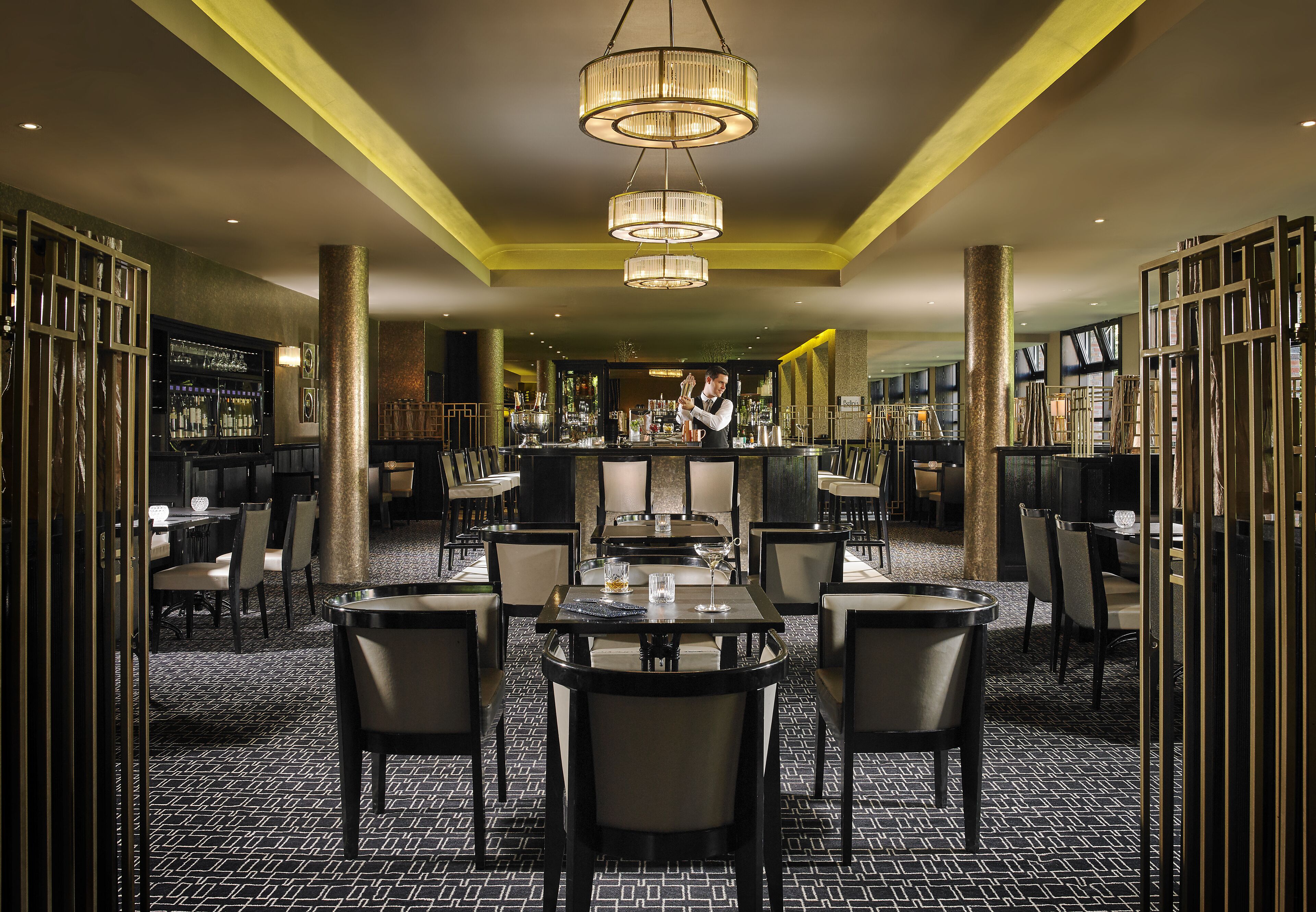 A restaurant with a bar area, multiple tables and chairs, and a chandelier.